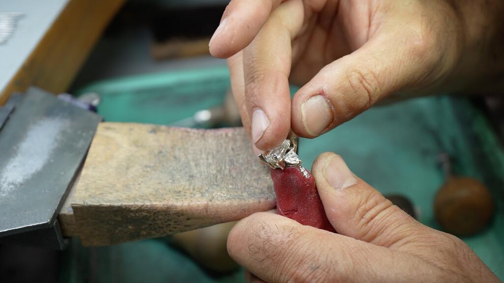 Hand holding diamond ring at jeweler bench