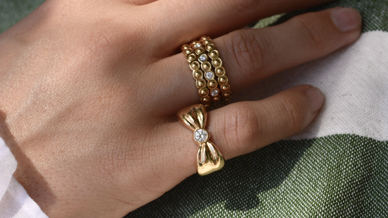 A stack of “Mini Eyelet Rings” in 18-karat yellow gold ($810) with “Mini Eyelet Diamond Ring” in 18-karat yellow gold and diamonds ($2,595) and a “Bow Ring” in 18-karat yellow gold and diamond ($2,850)